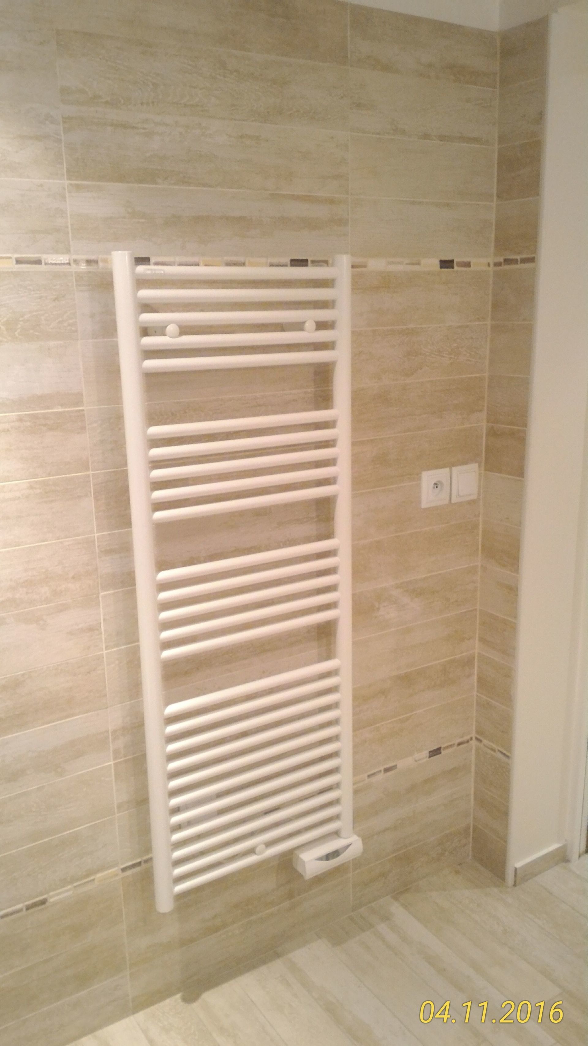 Chauffe-serviettes blanc monté sur un mur de salle de bain carrelé.