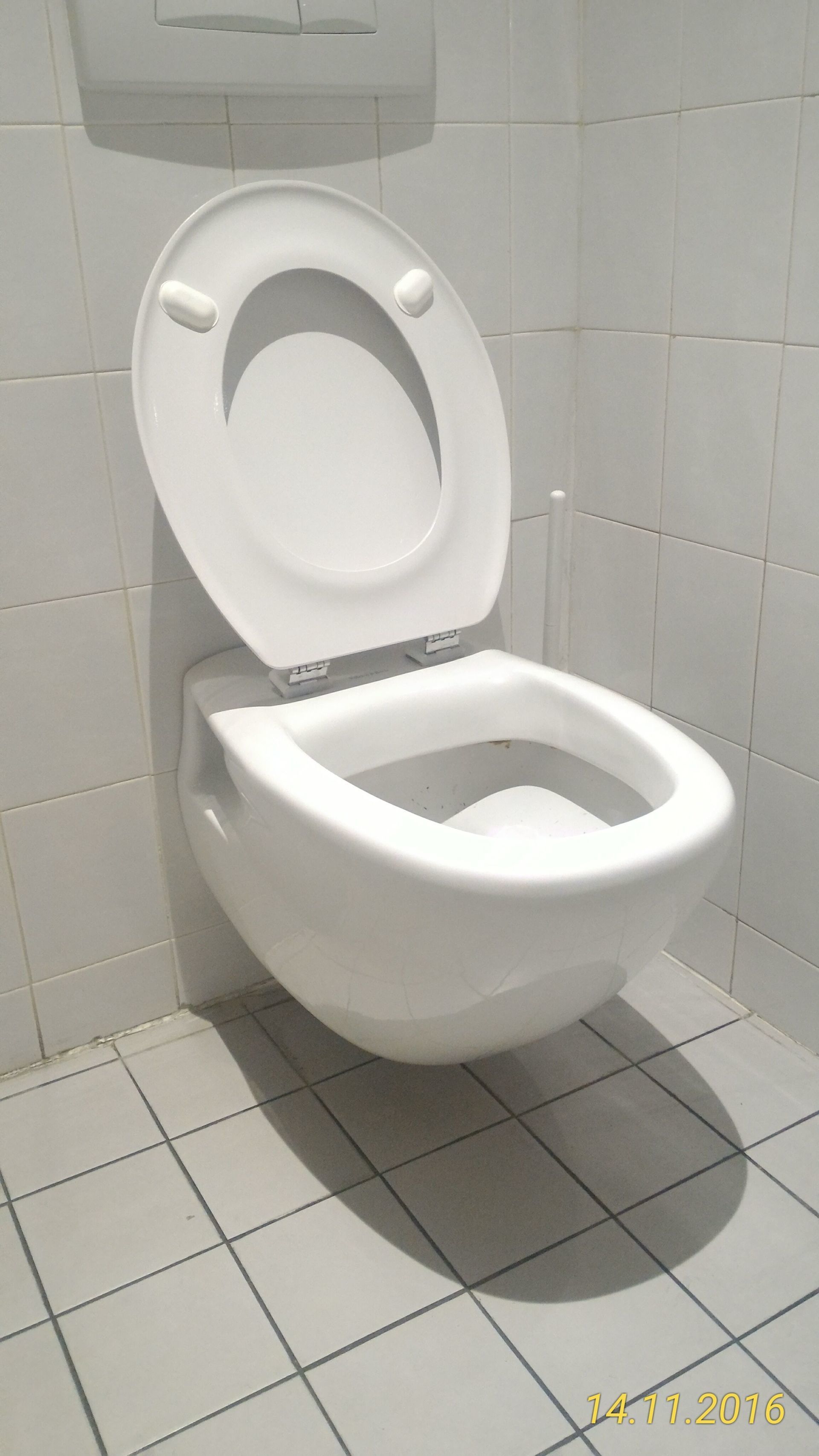 Toilettes murales blanches avec couvercle relevé dans une salle de bain carrelée.