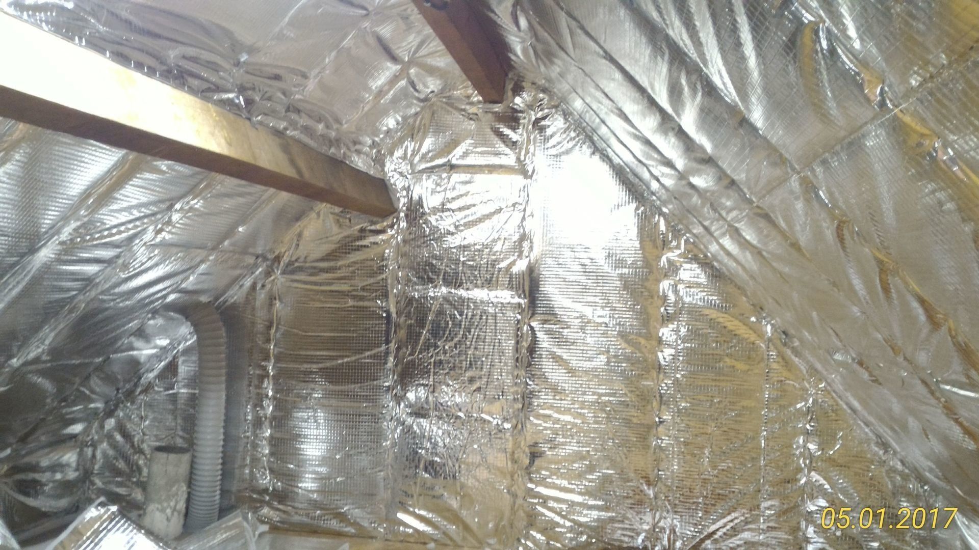Isolant réfléchissant argenté installé dans un grenier. Une poutre en bois est visible.