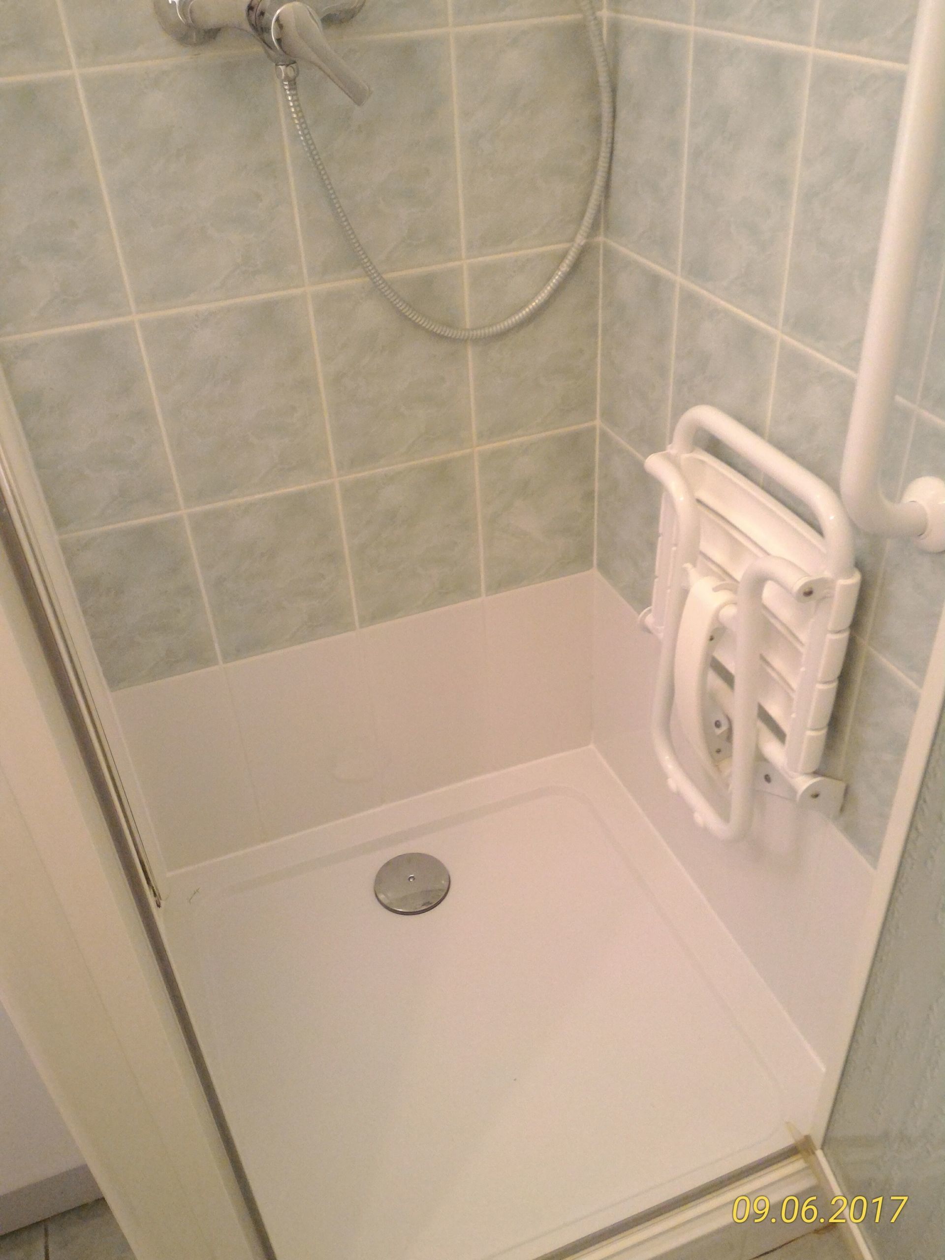 Cabine de douche accessible avec siège rabattable, base blanche, carrelage bleu pâle.