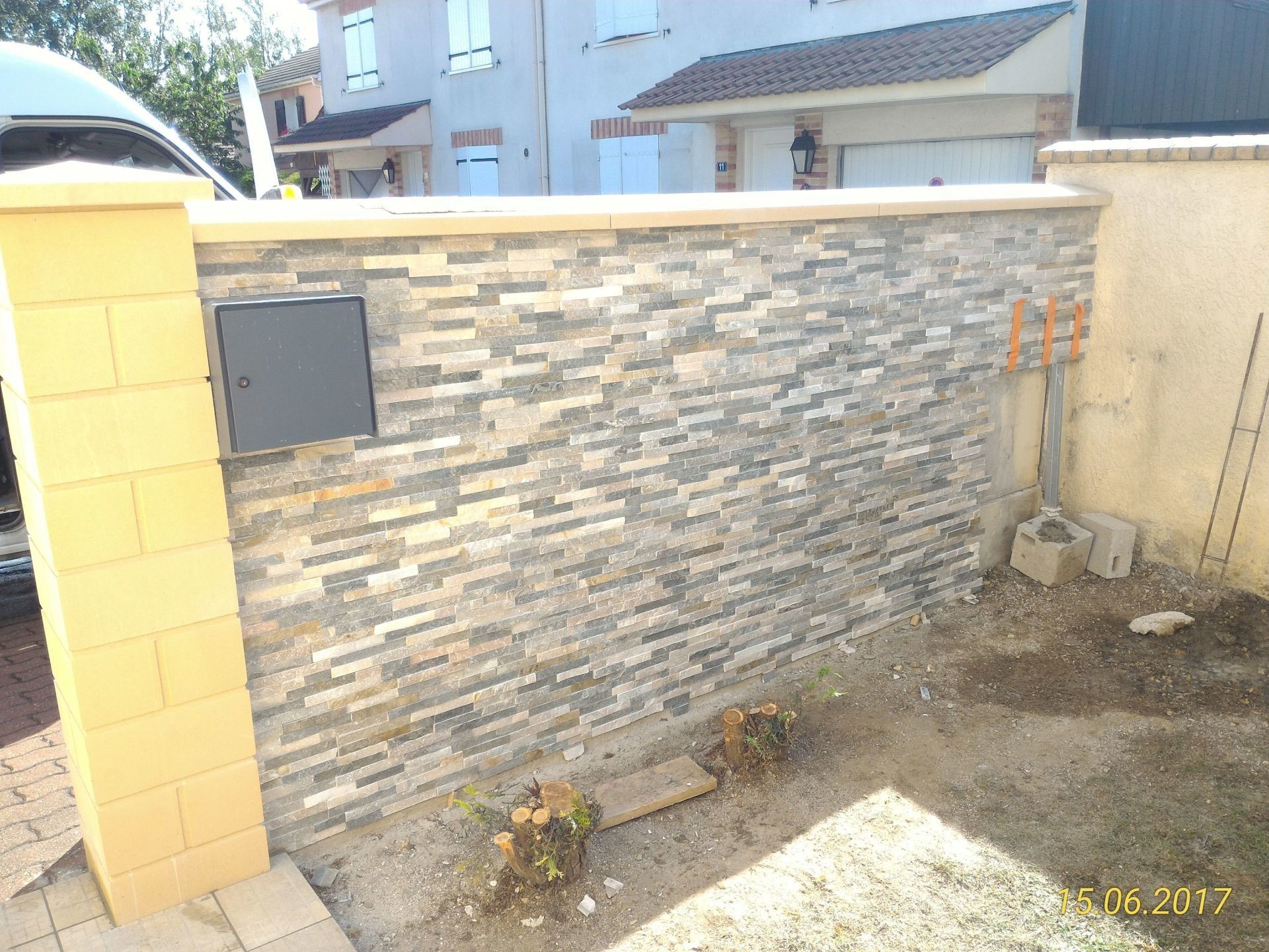 Façade en pierre avec une boîte aux lettres, à côté d'un pilier jaune et d'un mur beige.