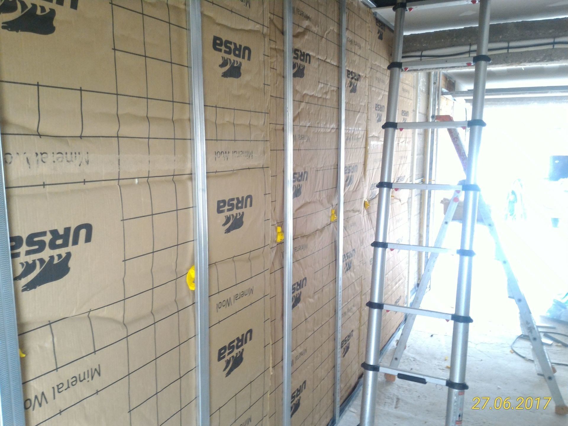 Isolation installée sur des montants sur un chantier. Une échelle est appuyée contre le mur.