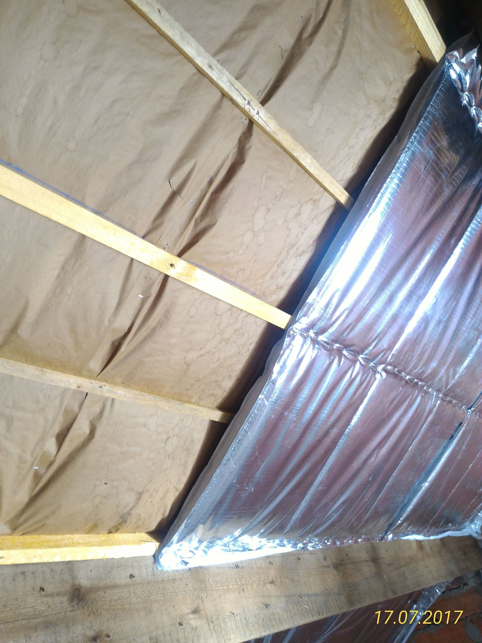 Grenier avec poutres en bois et isolation. Une partie est isolée par un film réfléchissant. Couleurs marron et argent.