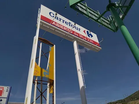 Letrero del supermercado Carrefour en azul, blanco y rojo contra un cielo despejado.