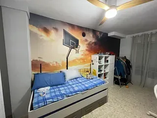 Dormitorio con mural con temática de baloncesto, cama individual con ropa de cama azul, mueble de almacenaje blanco y perchero.