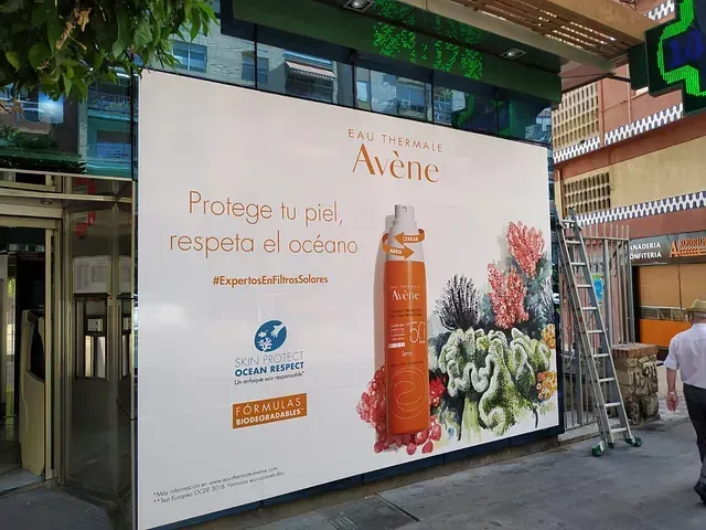 Gran anuncio exterior de Avene: botella de protector solar de color naranja con ilustraciones de arrecifes de coral; el texto dice: