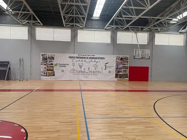 Gimnasio cubierto con suelo de madera y una pancarta colocada en el centro, con un aro de baloncesto al fondo.