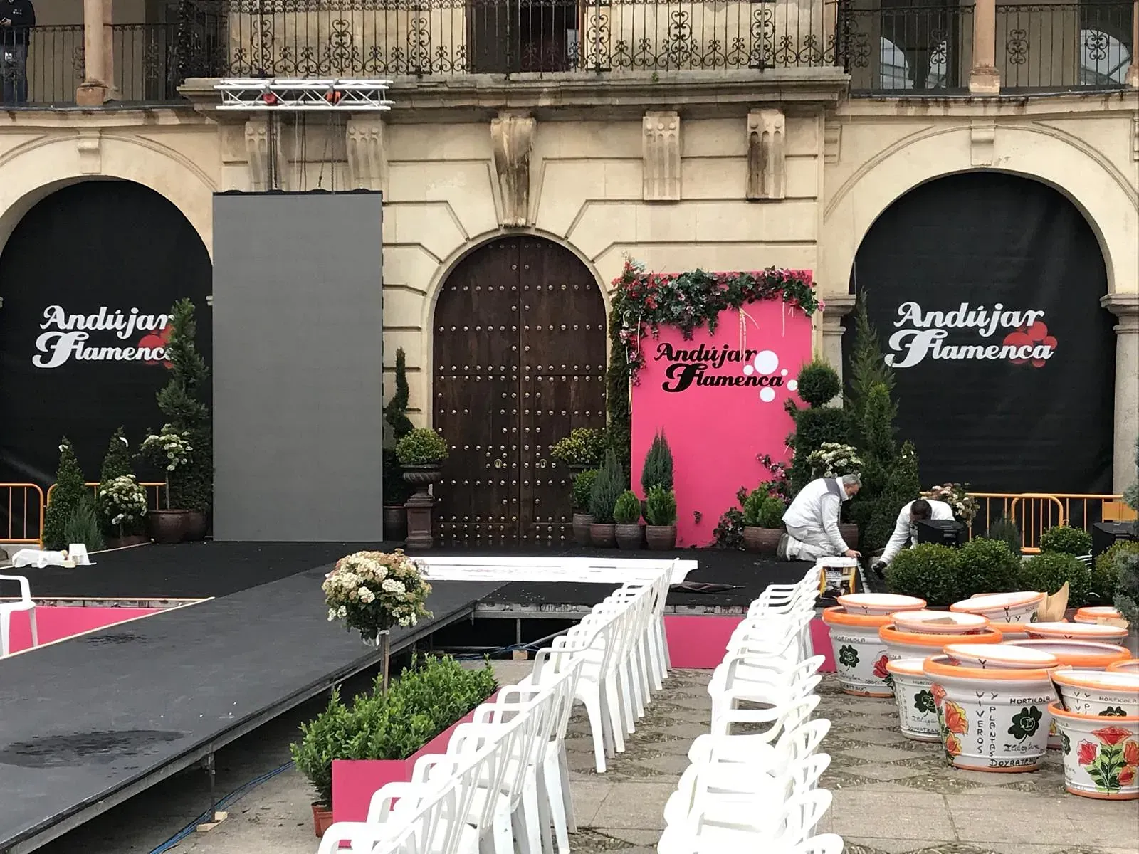 Montaje de escenario al aire libre para el evento "Andújar Flamenco". Fondo floral rosa y pasarela con sillas blancas.