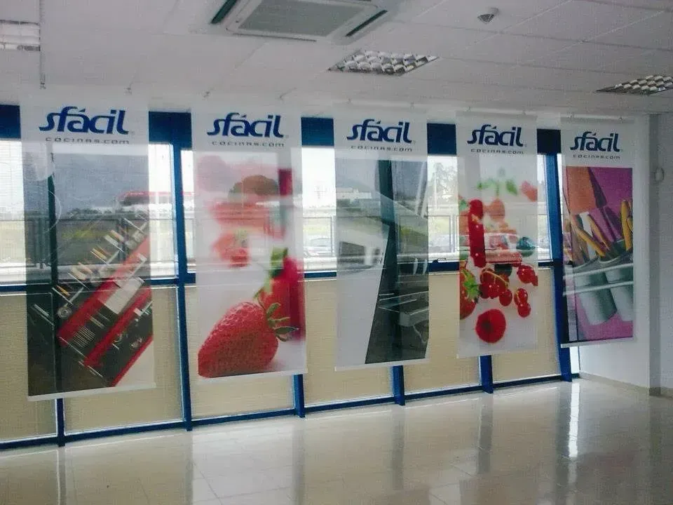 Delante de una ventana se exhiben pancartas con el logo "sfacil" e imágenes coloridas de artículos de cocina y fresas.