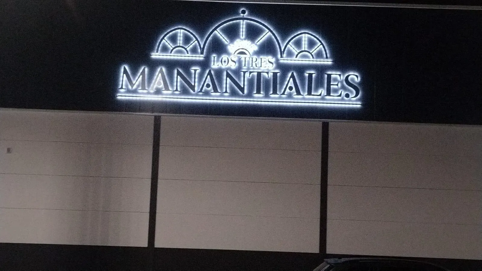 Letrero de neón brillante para "Los Tres Manantiales" con tres diseños de ruedas arqueadas.