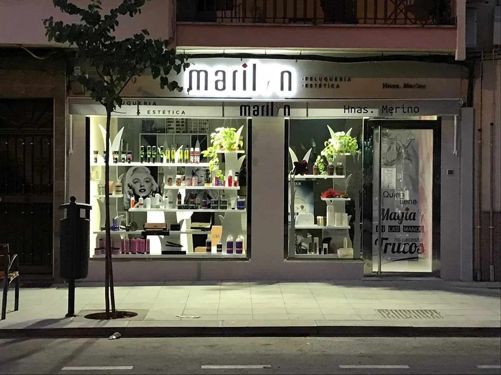 Exterior de un salón de belleza, "Mariln". El escaparate presenta un escaparate con productos de belleza y una imagen de Marilyn Monroe, iluminada por la noche.