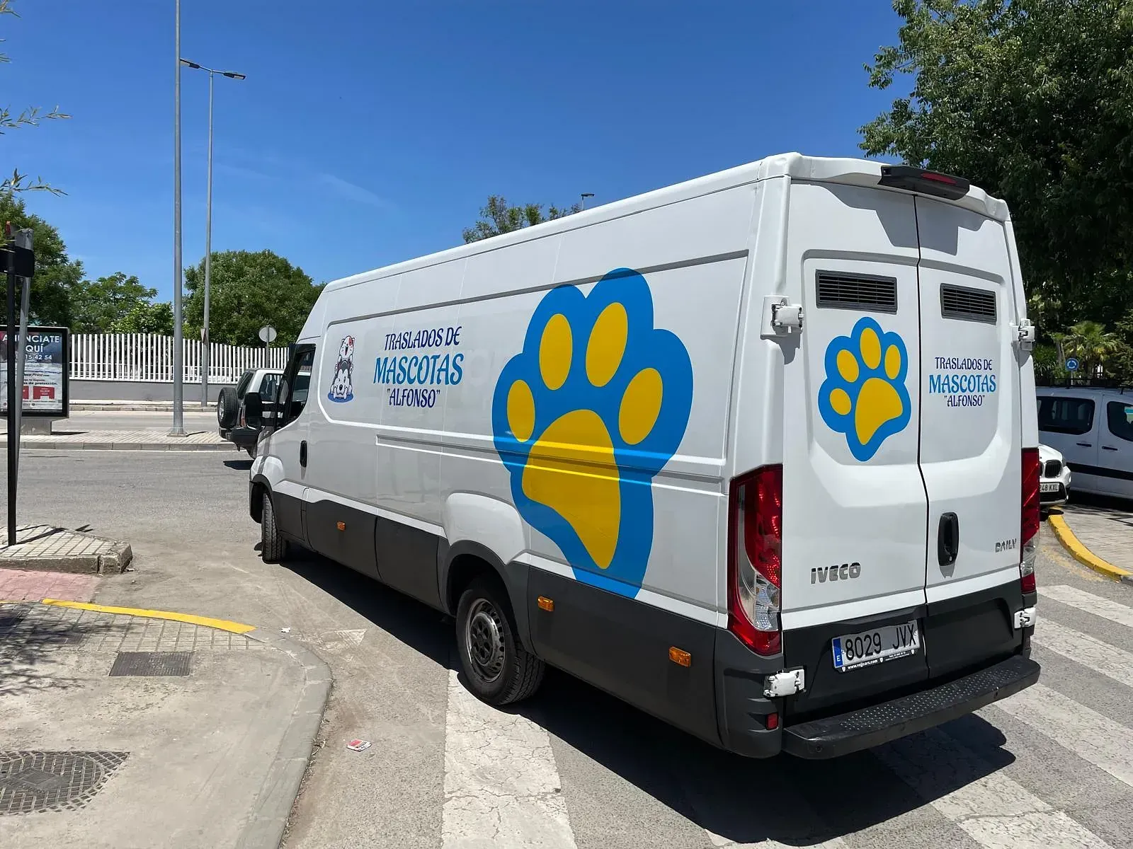 Una furgoneta blanca con el logo de una huella azul y amarilla estacionada en una esquina. La furgoneta lleva la inscripción "Asociación" en un lateral.