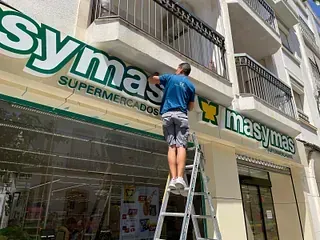 Un hombre en una escalera está instalando o reparando un cartel verde y blanco de