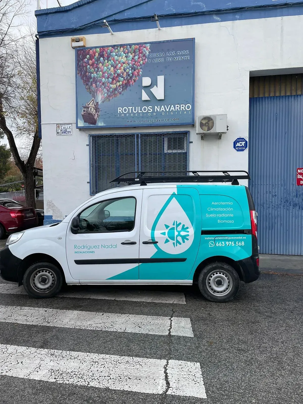 Una camioneta blanca y verde azulado con el logo "Rotulos Neward" estacionada frente a un edificio con el mismo logo.