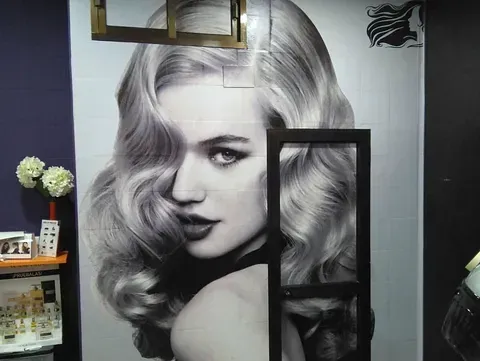 Retrato en blanco y negro de una mujer con cabello ondulado y voluminoso, probablemente un anuncio de peluquería. Mira por encima del hombro con expresión neutra.