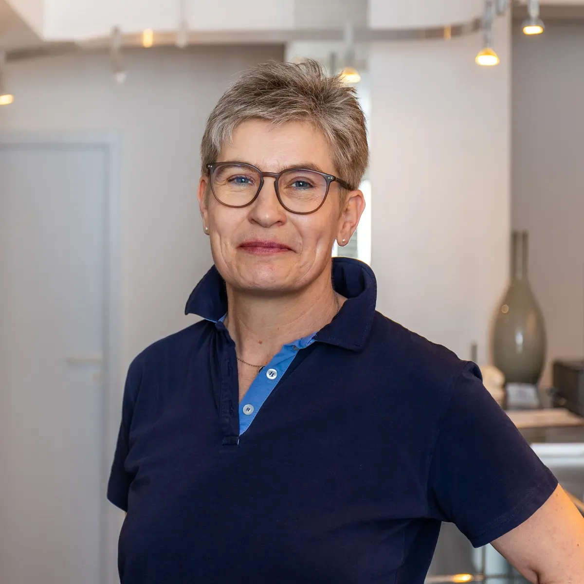Eine Frau mit Brille und blauem Hemd lächelt in die Kamera