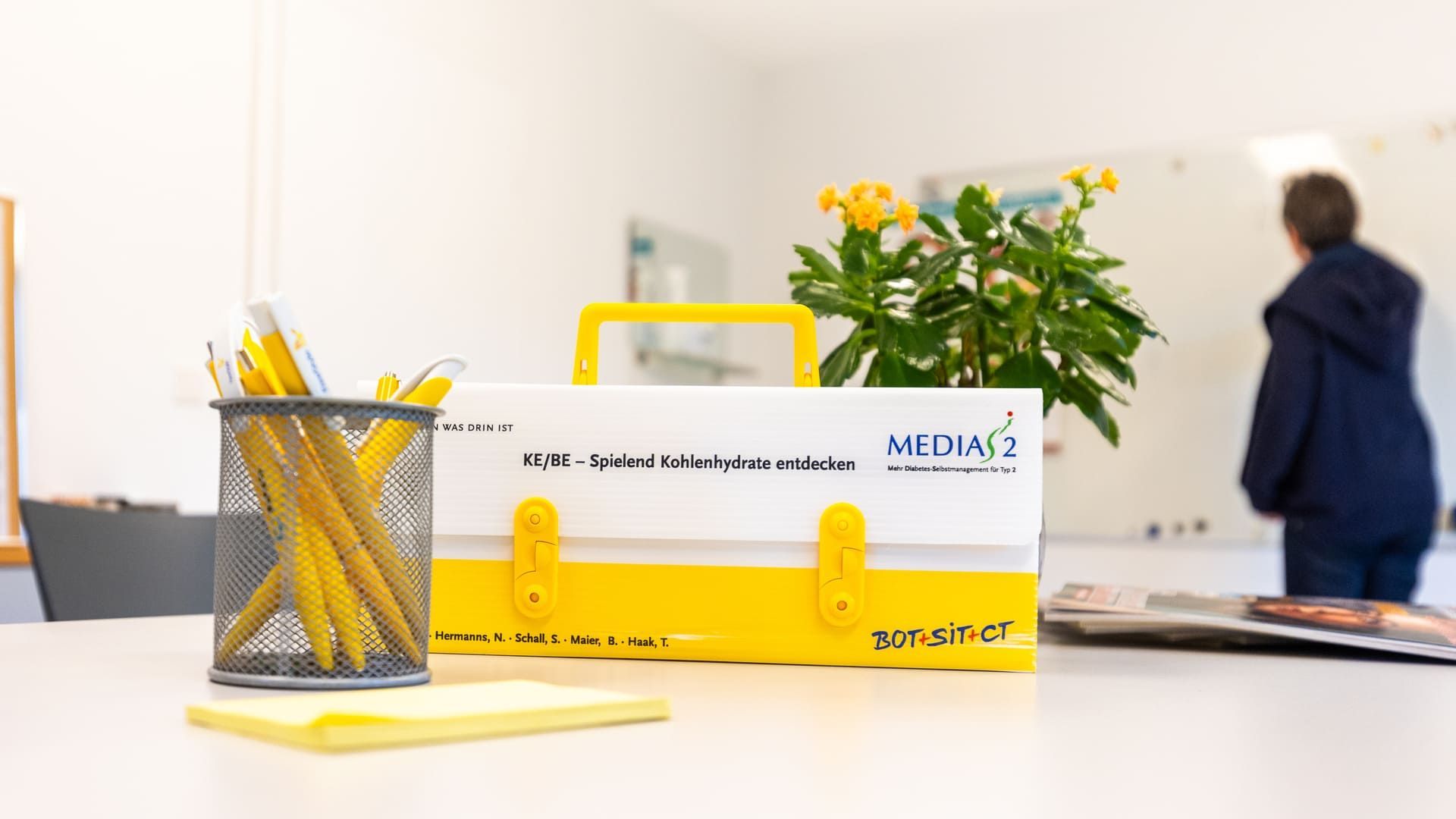 Ein gelber Werkzeugkasten steht neben einem Bleistifthalter auf einem Tisch.