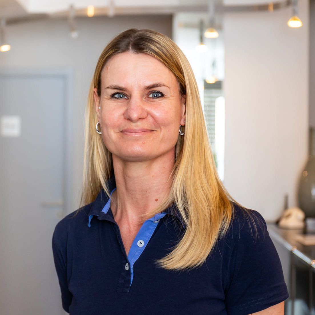 Eine Frau in einem blauen Poloshirt lächelt in die Kamera.