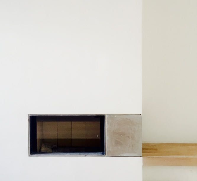 Una chimenea está empotrada en una pared blanca al lado de un estante de madera.