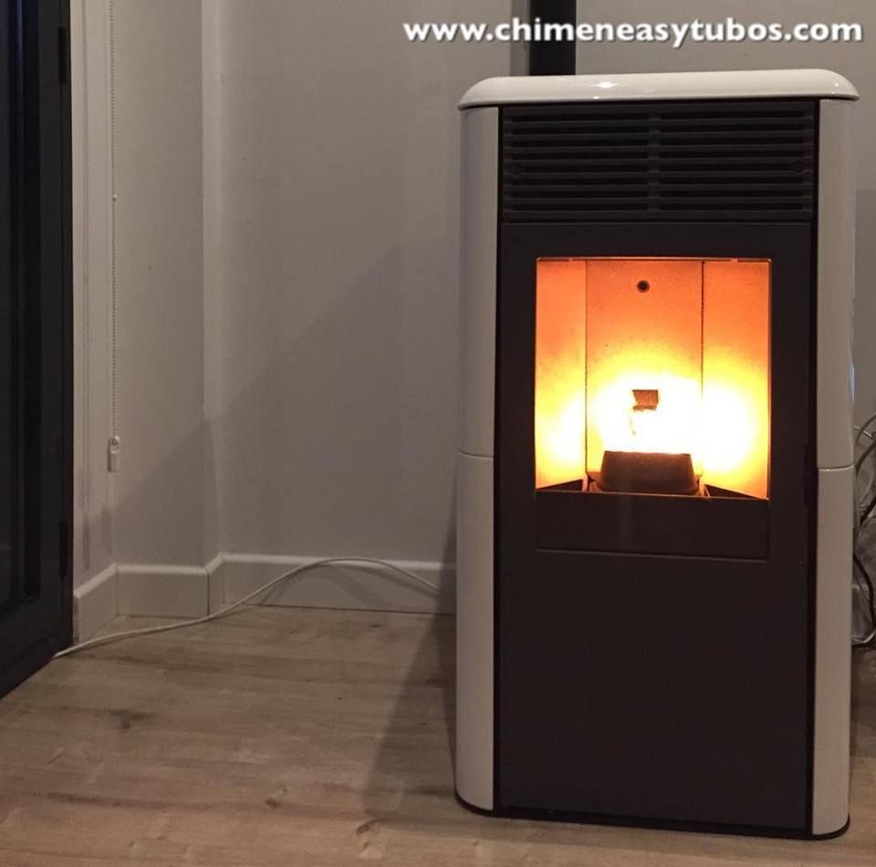 Una estufa de pellets blanca está colocada sobre un suelo de madera en una habitación.