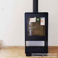 Una estufa de leña negra con puerta de cristal está colocada sobre un suelo de baldosas.