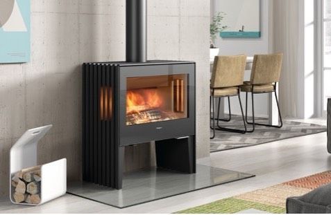 Una estufa de leña está ubicada en una sala de estar al lado de una mesa y sillas de comedor.