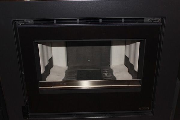 Una chimenea negra con puerta de cristal y moldura de acero inoxidable.