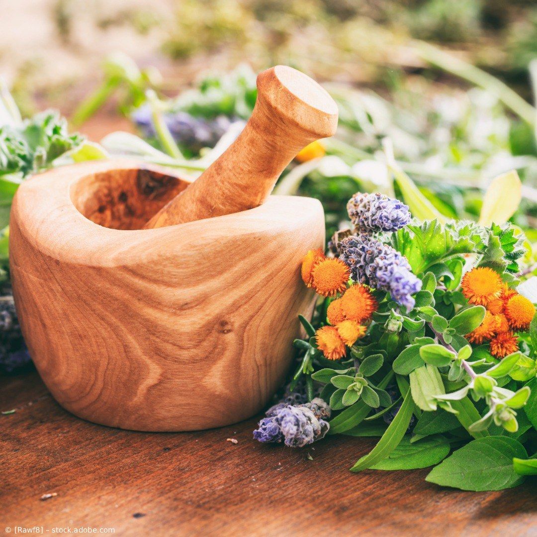 Ein hölzerner Mörser mit Stößel neben frischen Wildblumen auf einem rustikalen Tisch