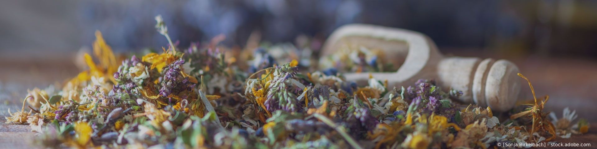 Getrocknete Blumen und ein Holzhammer mit weißem Griff auf einem rustikalen Tisch, beleuchtet von warmem Licht