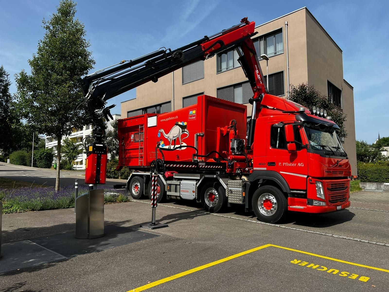 Ein roter LKW mit Kran parkt in der Nähe eines Gebäudes.