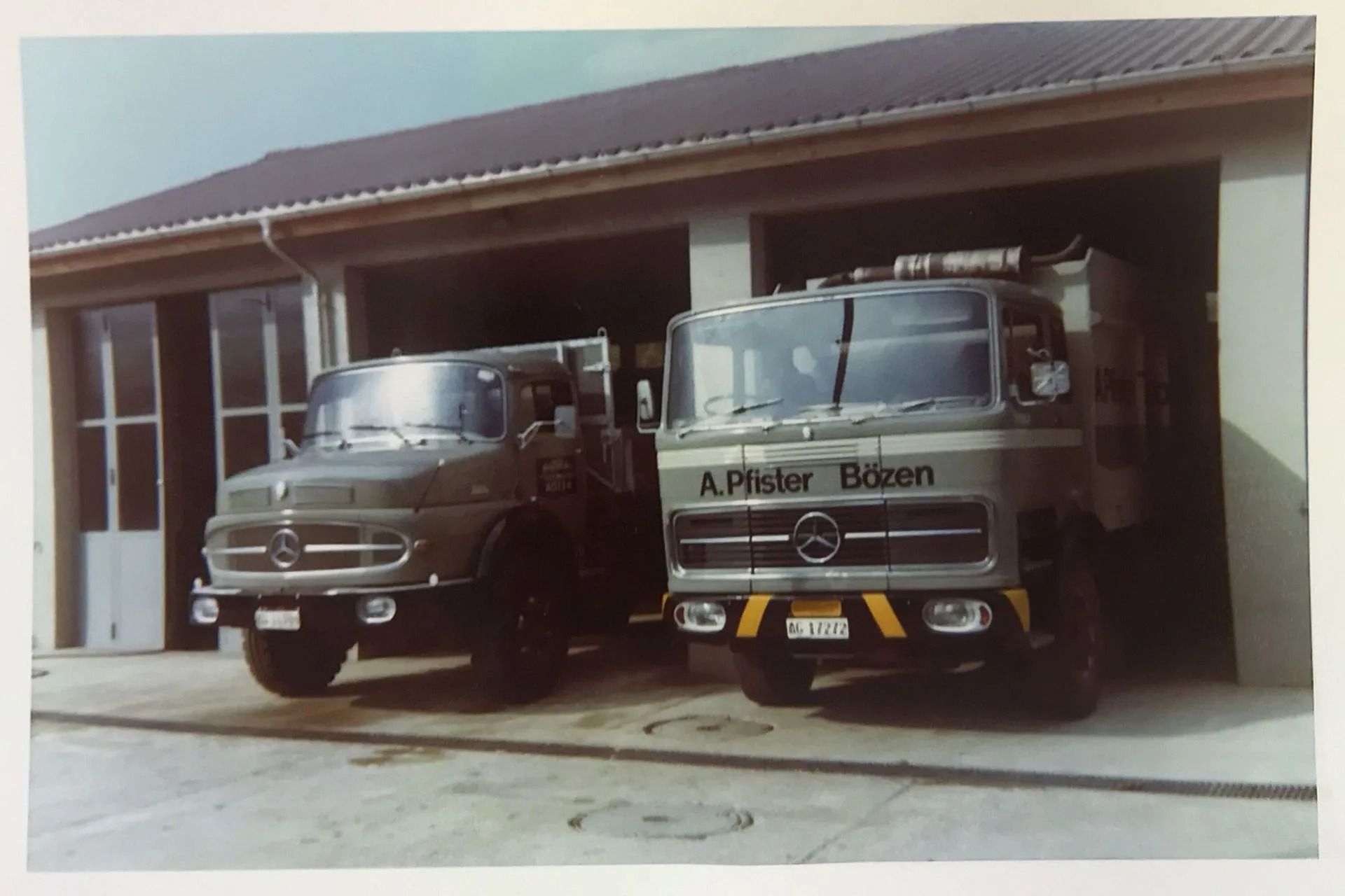 Zwei olivgrüne Mercedes-Lkw parkten vor einer Garage, einer mit der Aufschrift „A. Pfeifer Bözen“ an der Front.