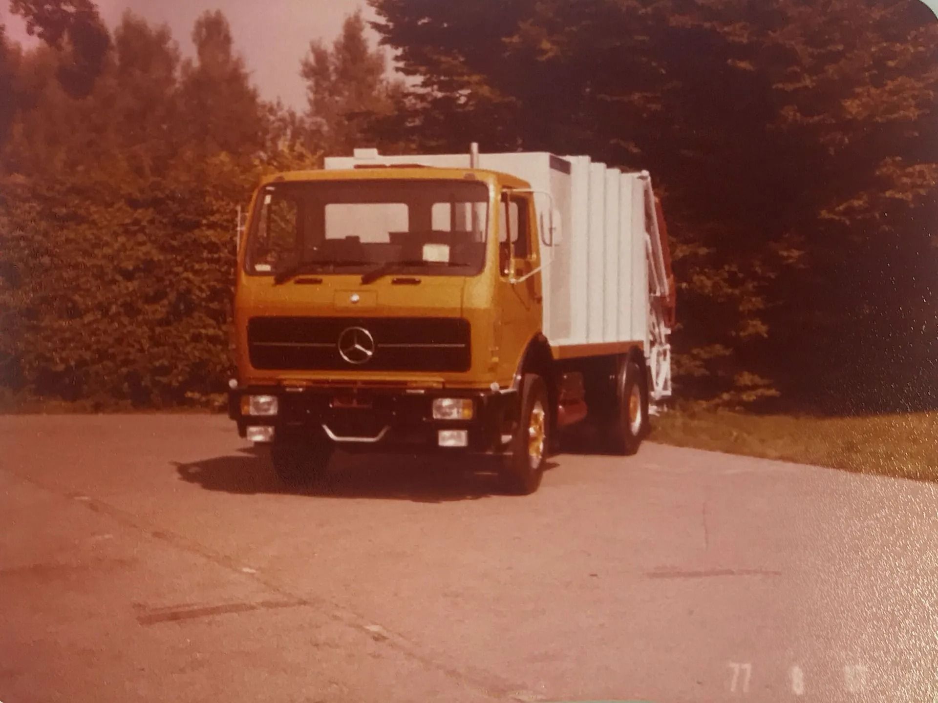 Ein gelber Mercedes-Müllwagen parkt auf dem Gehweg. Im Hintergrund sind Bäume zu sehen.
