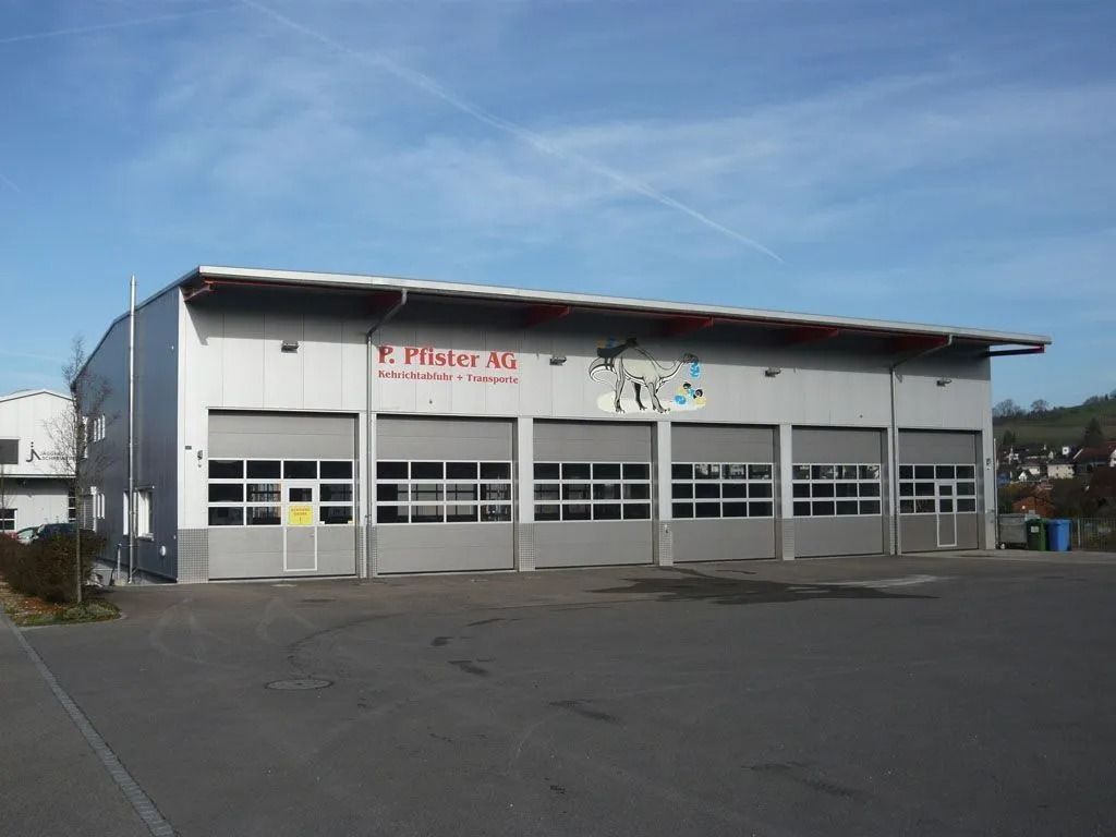 Aussenansicht eines Geschäftsgebäudes mit Garagentoren. Grau mit roten Akzenten und blauem Himmel.
