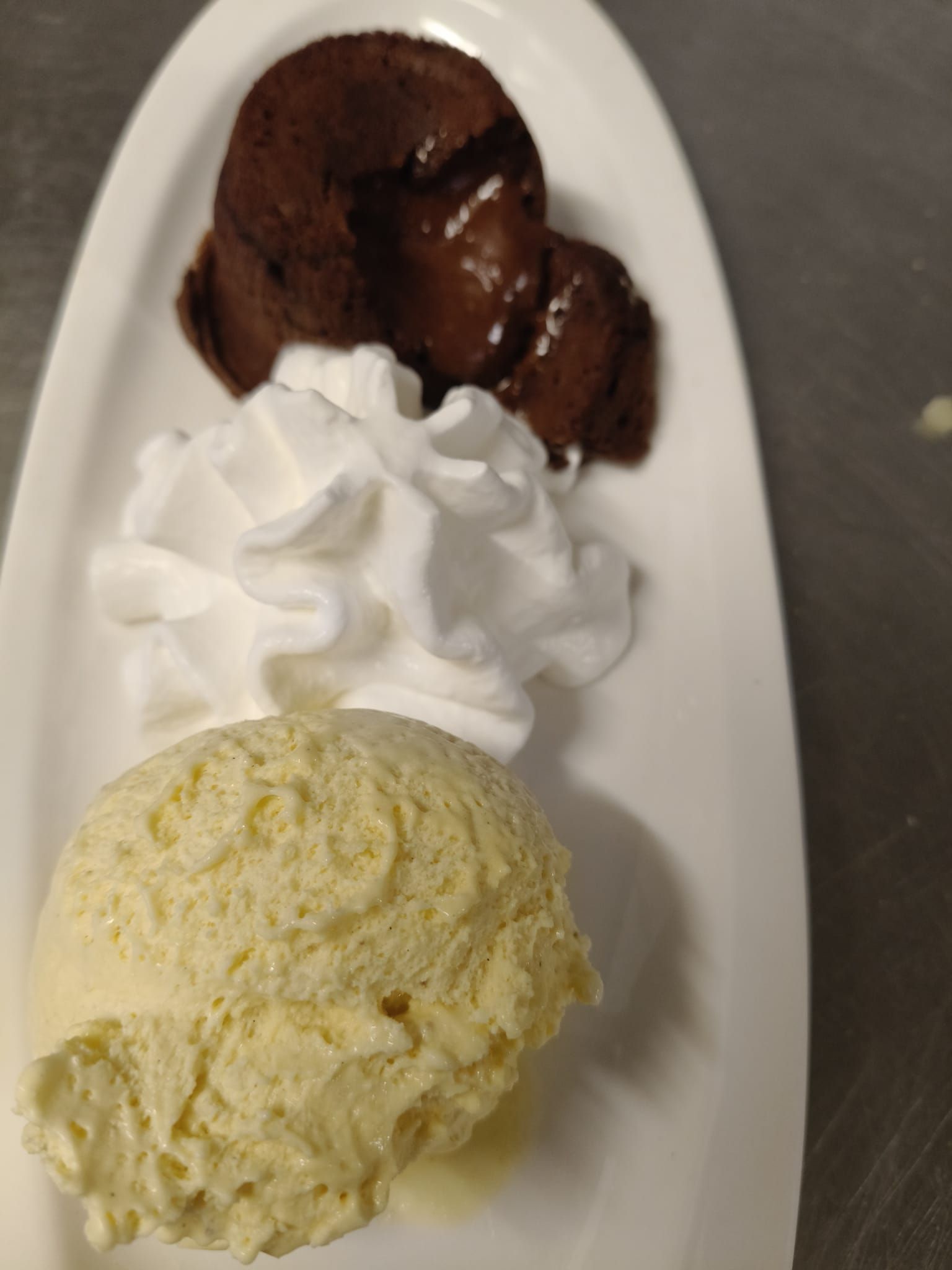 Pastel de lava de chocolate con crema batida y helado de vainilla en un plato blanco.