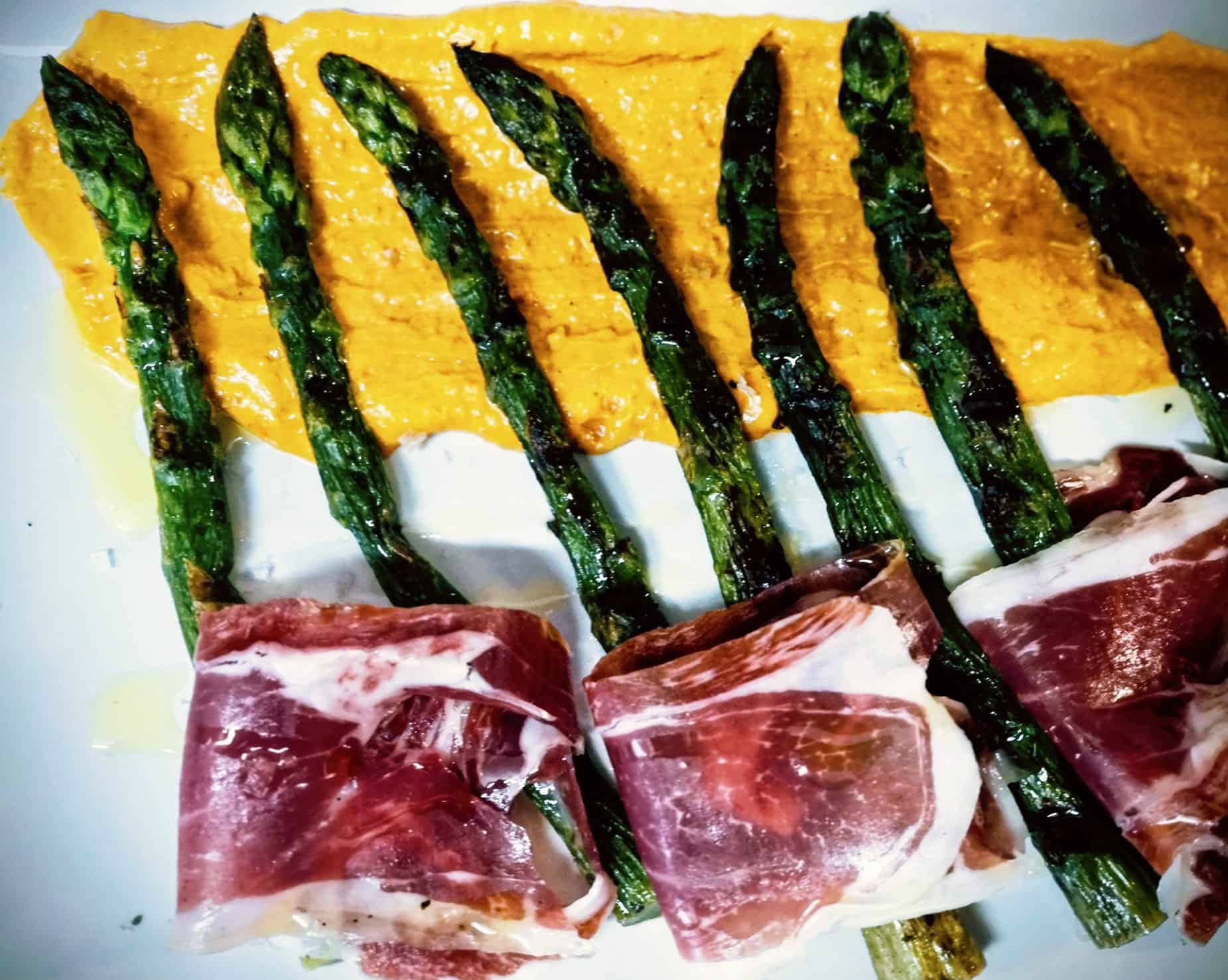 Platos de comida en una mesa con bebidas: carne a la parrilla y calamares con pan tostado, tomates, aceitunas y refresco.