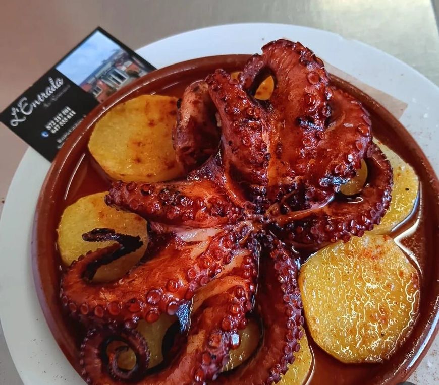 Platos de comida en una mesa con bebidas: carne a la parrilla y calamares con pan tostado, tomates, aceitunas y refresco.
