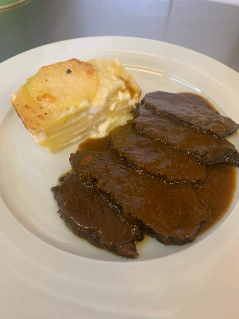 Guiso de carne, garbanzos y tomates en un recipiente de cerámica marrón sobre un plato blanco.