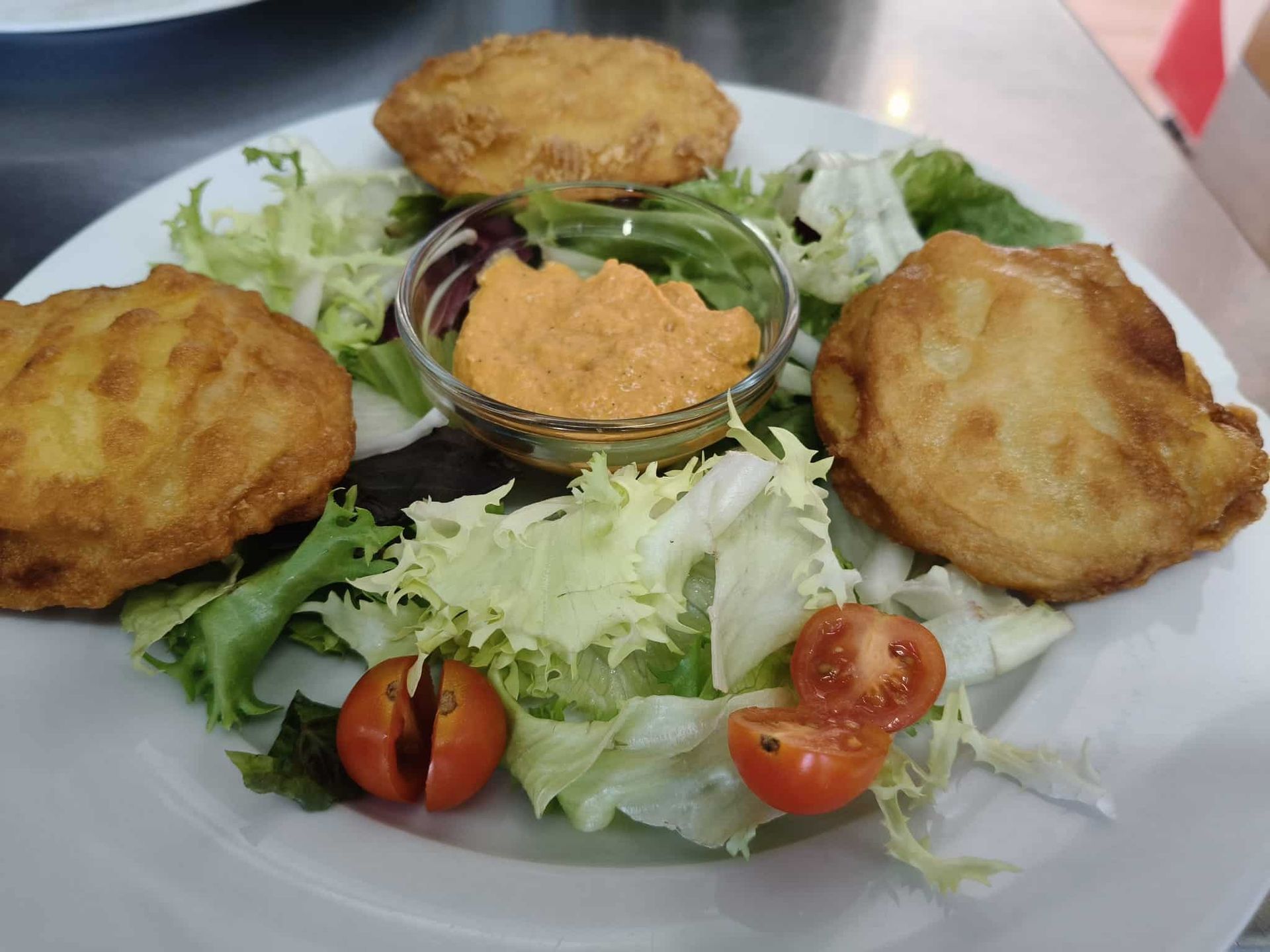 Ensalada de garbanzos, pollo desmenuzado, maíz y pimientos rojos sobre una cama de lechuga, en un plato blanco.
