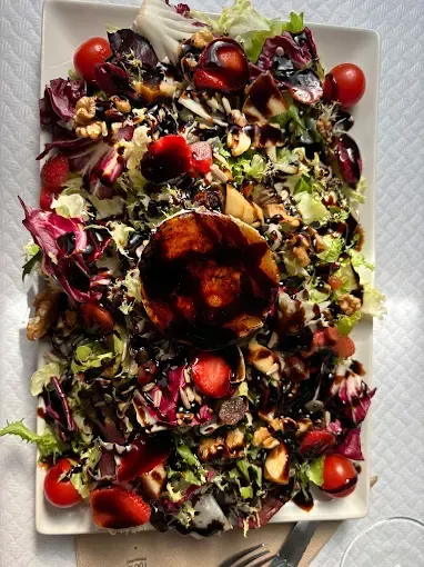 Ensalada en plato blanco: verduras mixtas, tomates, nueces, fresas y queso de cabra rociado con glaseado balsámico.