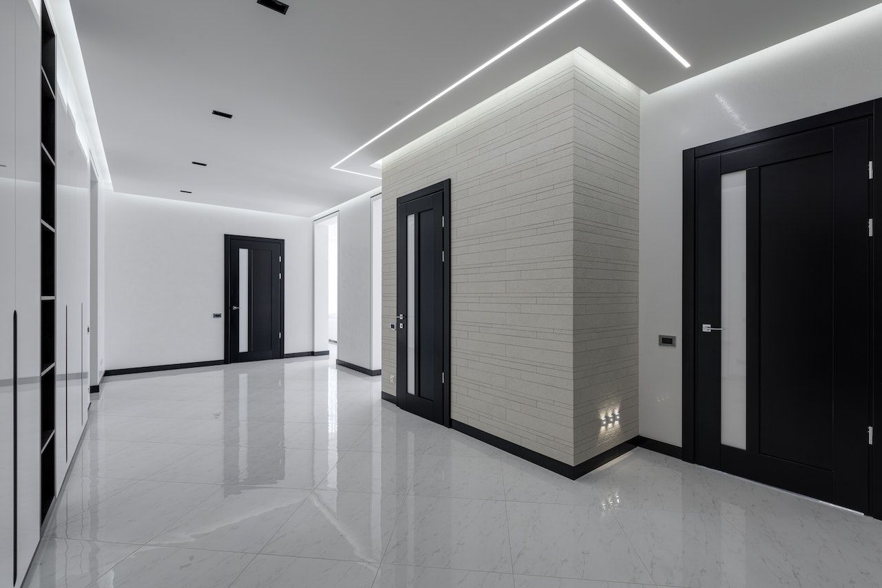Un pasillo vacío con puertas negras y una luz de techo.