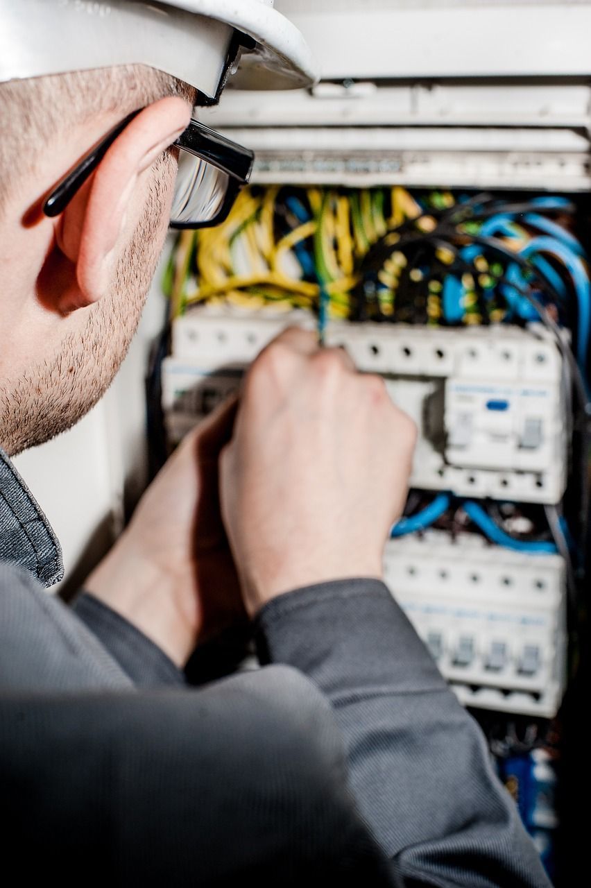 Un hombre que lleva casco y gafas de seguridad está trabajando en una caja eléctrica.