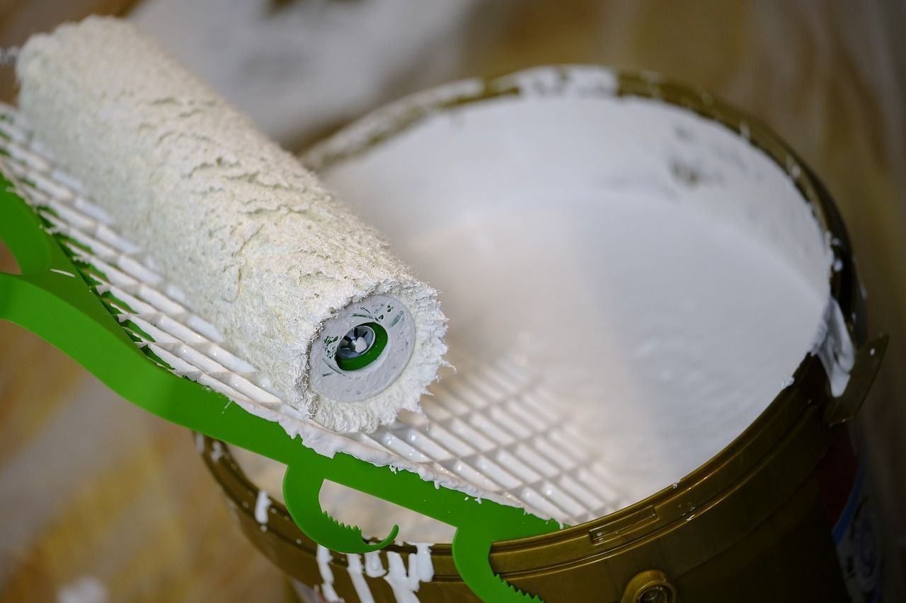 Un rodillo de pintura está colocado encima de un balde de pintura blanca.