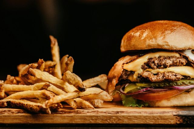 Una hamburguesa y papas fritas están en una tabla de cortar de madera.