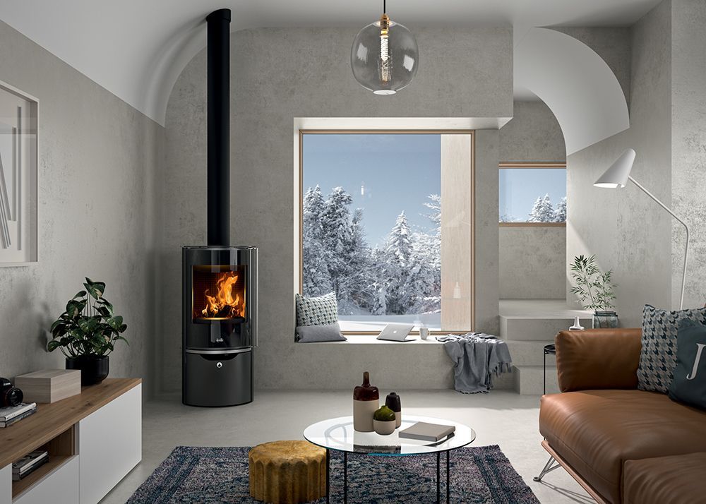 Salon moderne avec cheminée, canapé en cuir marron et grande fenêtre donnant sur un paysage hivernal enneigé.