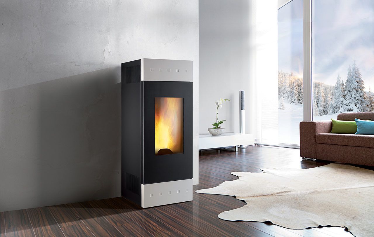 Un poêle à granulés moderne, noir et argent, crache une flamme vive dans un salon contemporain offrant une vue sur un paysage enneigé.