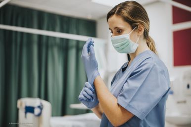 Pflegerin zieht sich einen Hygienehandschuh an
