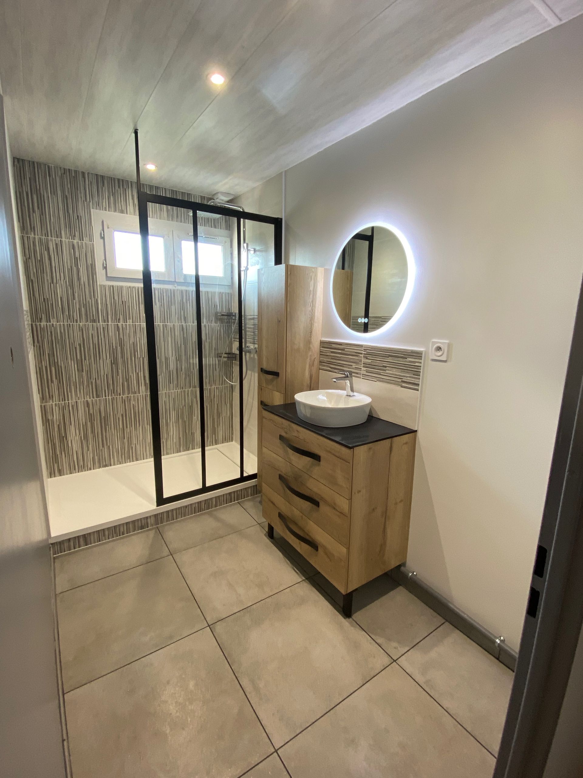 Vue sur une douche à l'italienne contemporaine, une vasque sur meuble en bois et un miroir LED