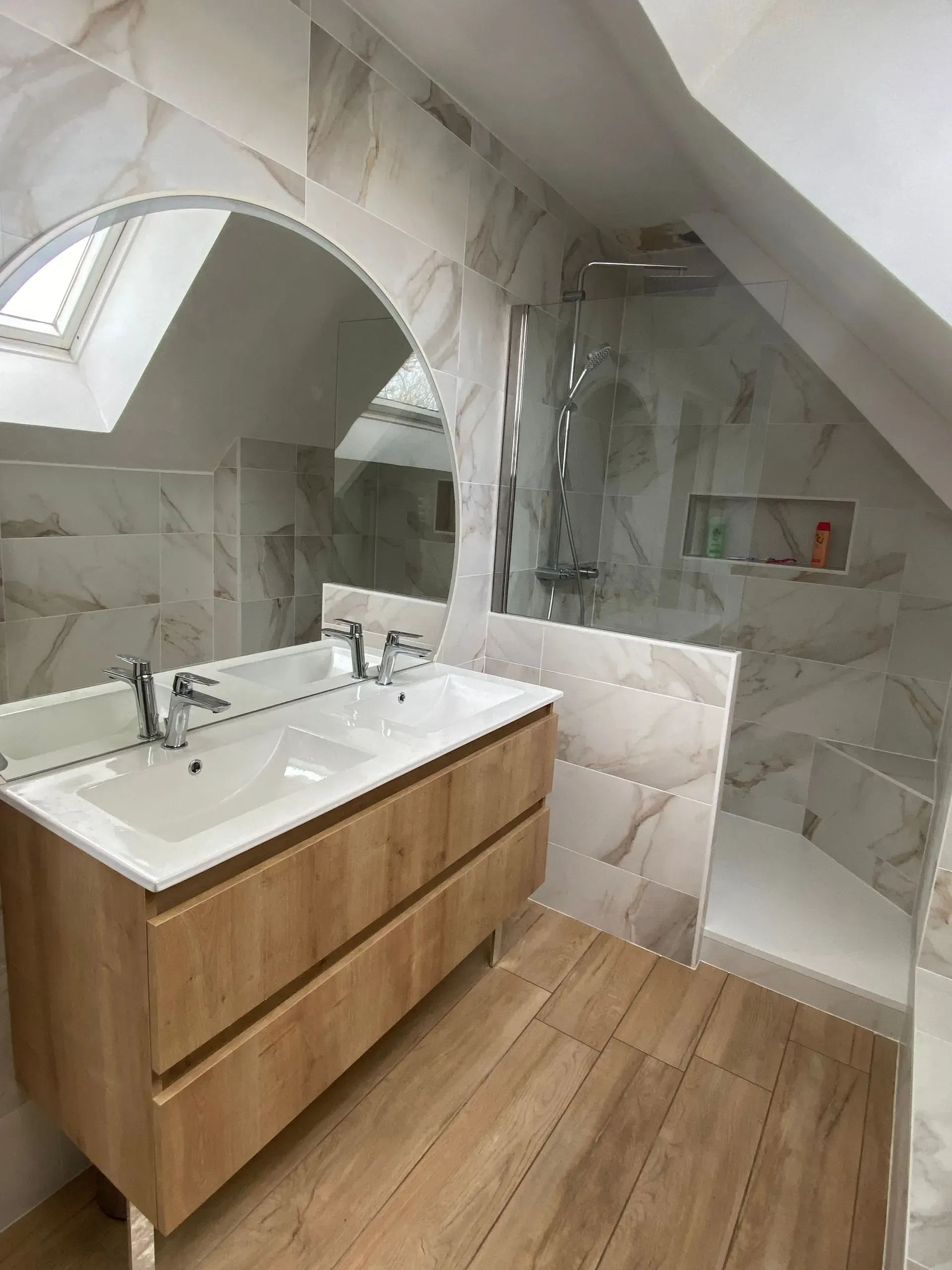 Salle de bains sous pente après rénovation : vue sur le meuble double vasque, le miroir et le coin douche