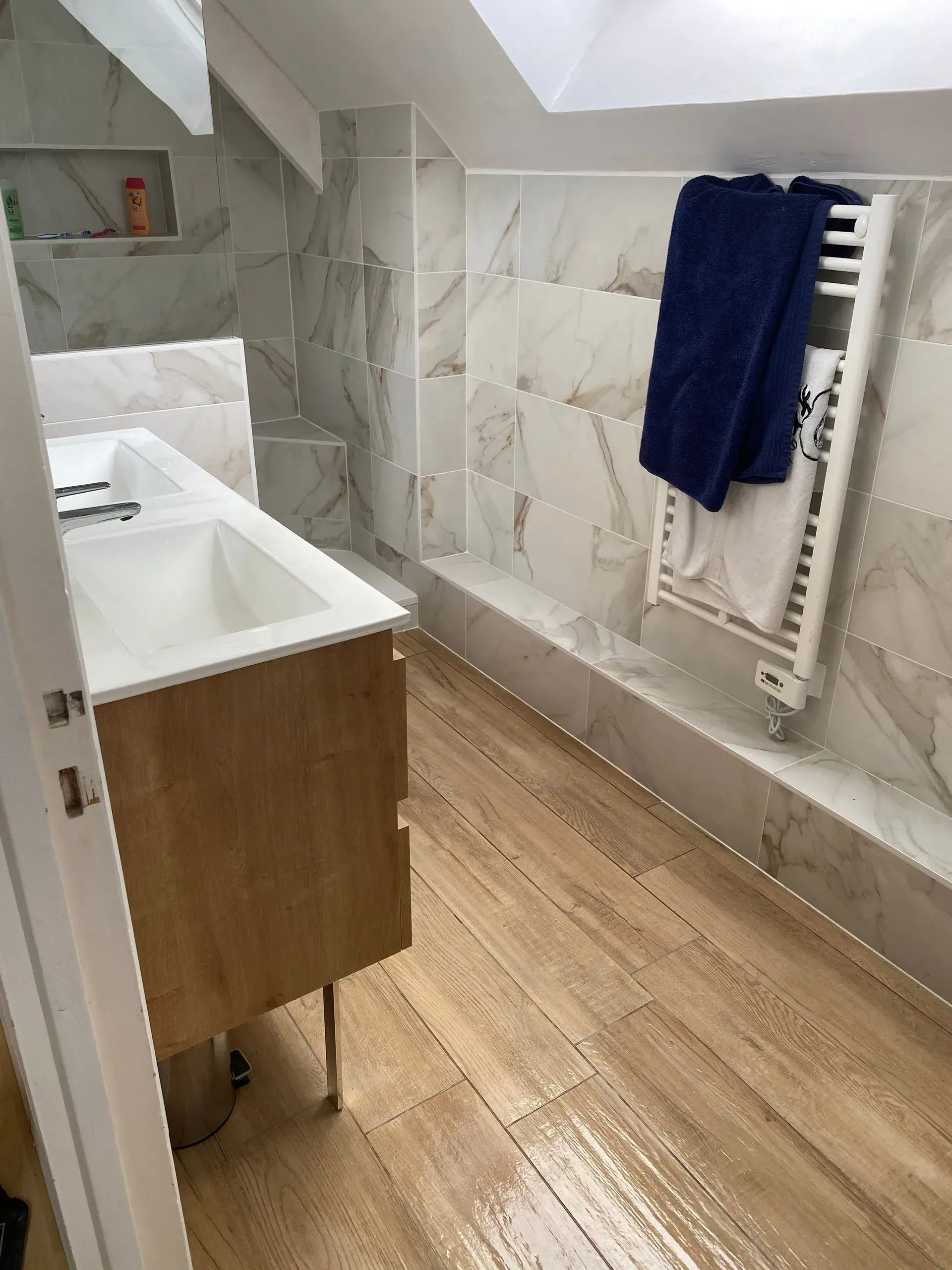 Salle de bains sous pente après rénovation : vue sur le meuble vasque, le sèche-serviettes et le sol