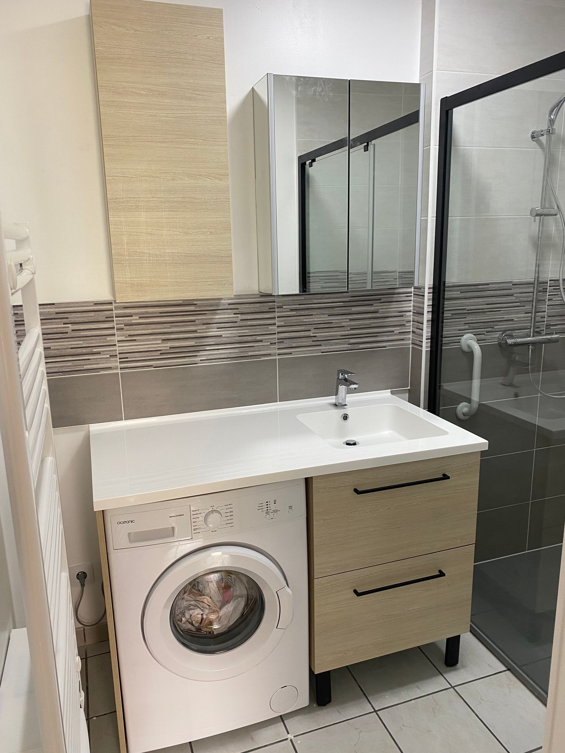 Salle d'eau après travaux avec un lave-linge, un meuble vasque, un miroir et une cabine de douche